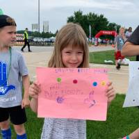 Child from the GVSU Children's Enrichment Center smiling and holding a cheerful to encourage racers